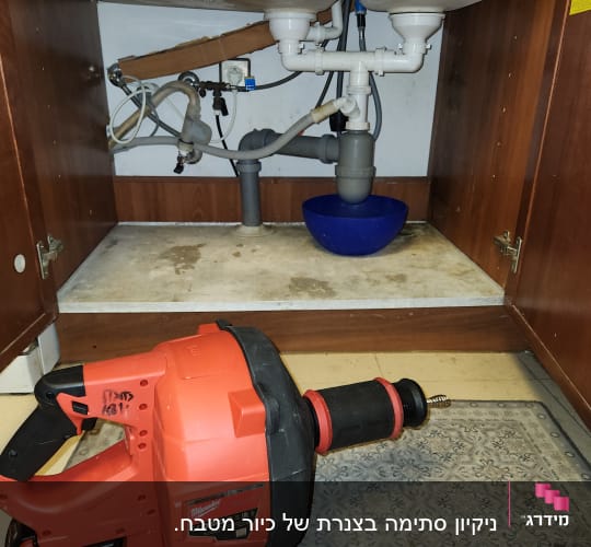 כלי עבודה אדום ליד כיור עם צנרת מתחת
